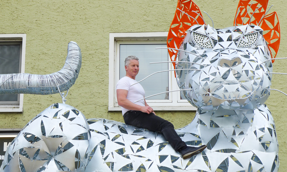 Künstler Matthias Mauritz sitzt auf der fertigen Metallkatze vor dem Feuerverzinken